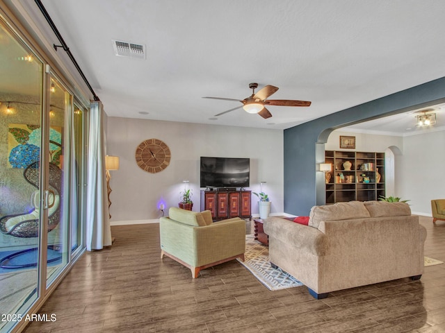 living room with dark wood-type flooring, ornamental molding, and ceiling fan