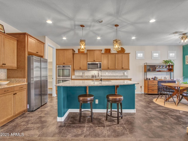 kitchen with decorative light fixtures, sink, light stone counters, stainless steel appliances, and a center island with sink