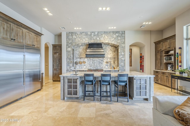 8248 E Arroyo Hondo Rd, Scottsdale, AZ 85266 - kitchen featuring arched walkways, built in appliances, light stone counters, a large island with sink, and premium range hood