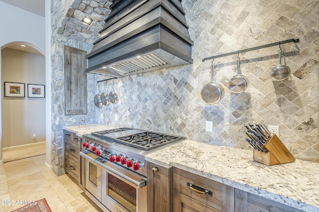 8248 E Arroyo Hondo Rd, Scottsdale, AZ 85266 - kitchen with premium range hood, range with two ovens, arched walkways, decorative backsplash, and light stone countertops