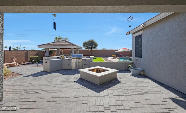 view of patio featuring an outdoor fire pit, an outdoor kitchen, a fenced backyard, area for grilling, and a gazebo