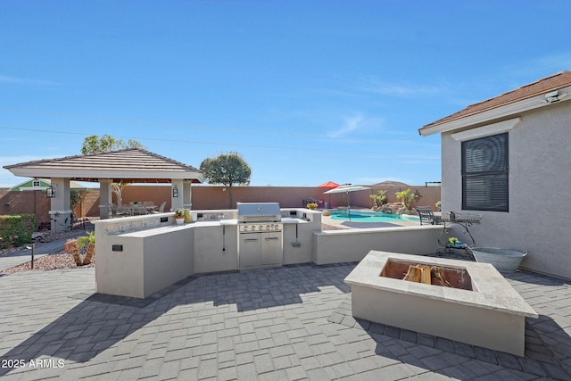 view of patio with an outdoor kitchen, a fenced backyard, a fire pit, a grill, and a gazebo