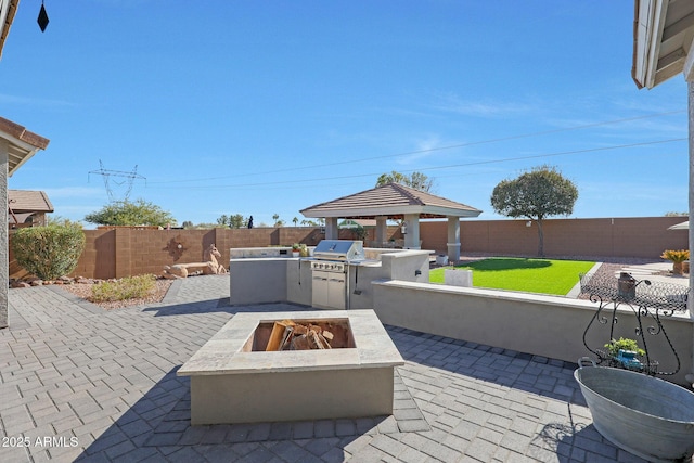 view of patio / terrace with a fenced backyard, a fire pit, a grill, a gazebo, and exterior kitchen