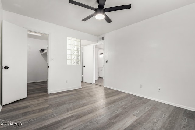 unfurnished bedroom with ceiling fan, a walk in closet, a closet, and dark hardwood / wood-style flooring