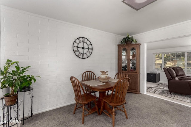 carpeted dining space with brick wall