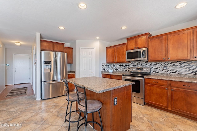 5305 E Silverbell Rd, San Tan Valley, AZ 85143 - kitchen featuring appliances with stainless steel finishes, a kitchen island, backsplash, brown cabinetry, and a kitchen breakfast bar