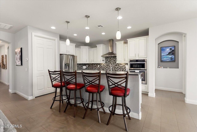 kitchen with appliances with stainless steel finishes, backsplash, wall chimney exhaust hood, pendant lighting, and white cabinetry