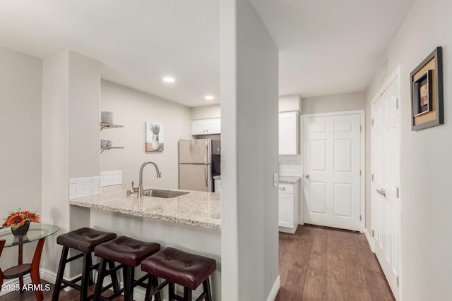 kitchen featuring a breakfast bar, decorative backsplash, freestanding refrigerator, white cabinetry, and a sink