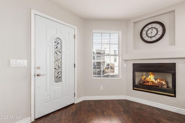 foyer entrance with dark wood-style flooring, a glass covered fireplace, and baseboards