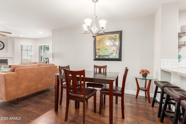 dining room featuring ceiling fan with notable chandelier, baseboards, dark wood finished floors, and a glass covered fireplace