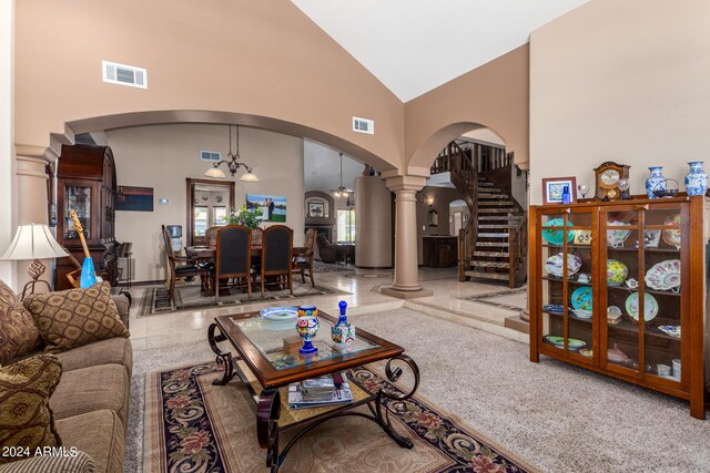 carpeted living room with a notable chandelier, high vaulted ceiling, and decorative columns