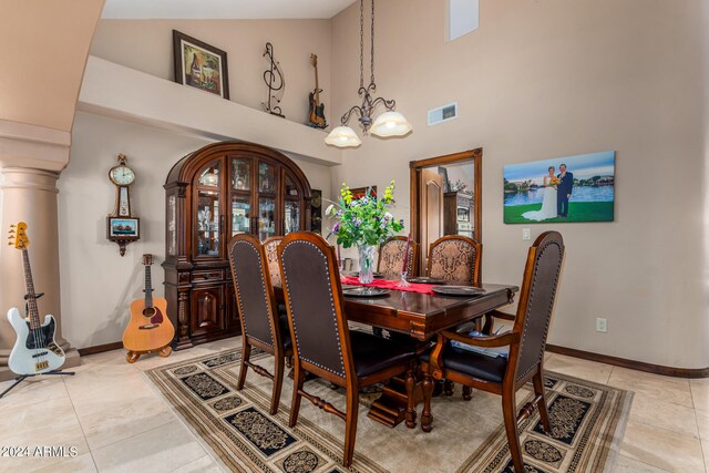 tiled dining area featuring decorative columns, high vaulted ceiling, and a chandelier