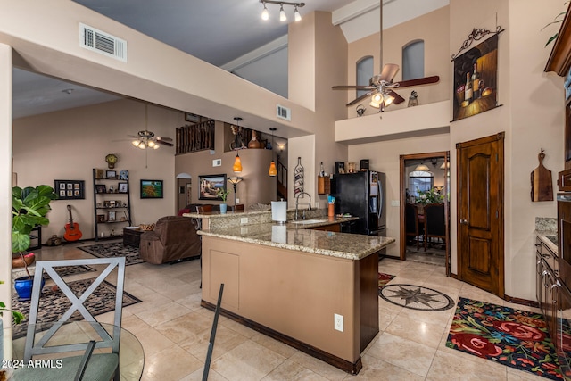 kitchen with hanging light fixtures, a kitchen island, sink, a high ceiling, and light stone counters