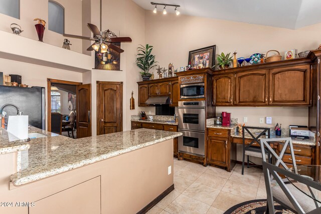 kitchen with light tile patterned floors, appliances with stainless steel finishes, ceiling fan, light stone countertops, and high vaulted ceiling