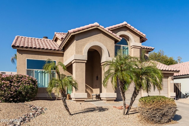 mediterranean / spanish house featuring a garage, a tile roof, and stucco siding