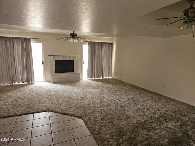 unfurnished living room with a textured ceiling, ceiling fan, a tiled fireplace, and light carpet