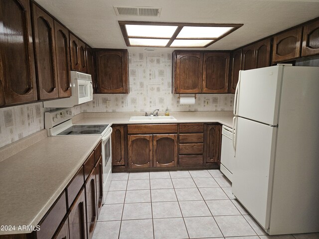 kitchen featuring white appliances, light tile patterned floors, dark brown cabinets, and sink