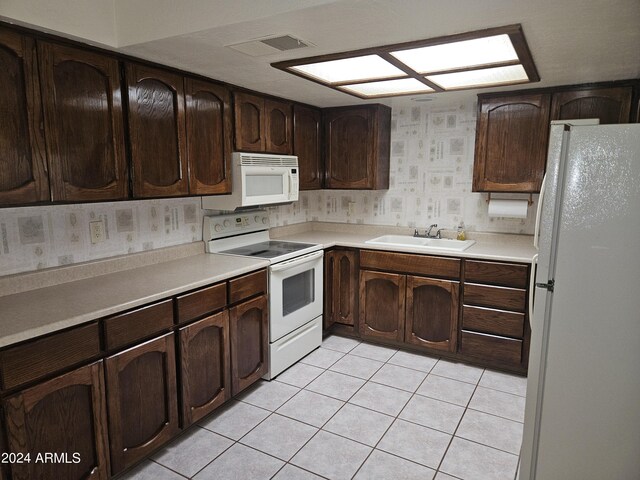 kitchen featuring sink, dark brown cabinetry, white appliances, and light tile patterned flooring