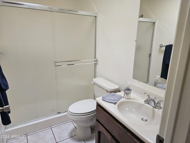 bathroom with a shower with door, vanity, toilet, and tile patterned floors