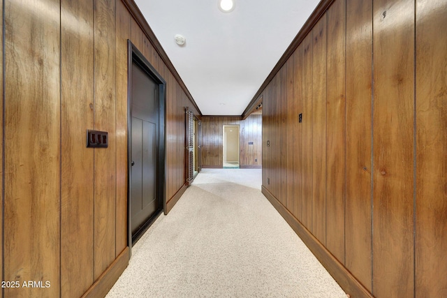 hallway with wood walls, crown molding, and light carpet