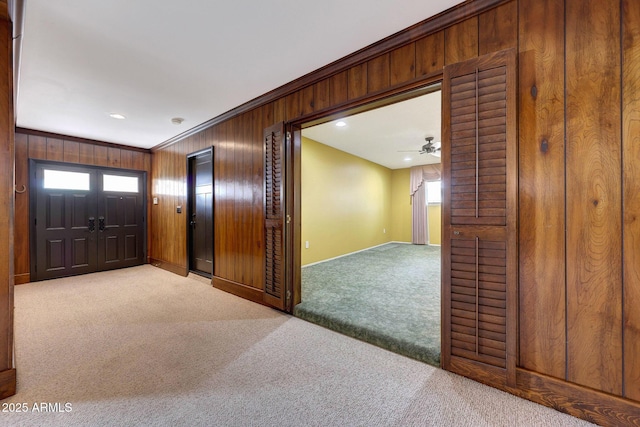 foyer entrance featuring carpet flooring, crown molding, wooden walls, and baseboards