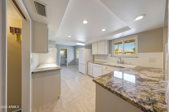 kitchen featuring visible vents, white appliances, white cabinetry, a sink, and light stone counters