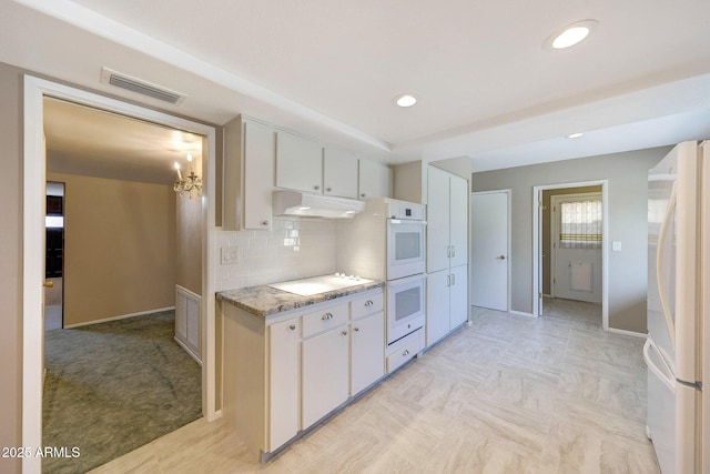 kitchen with backsplash, white cabinetry, under cabinet range hood, white appliances, and visible vents