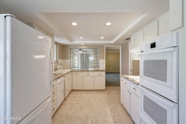 kitchen with a tray ceiling, recessed lighting, white appliances, decorative backsplash, and a sink