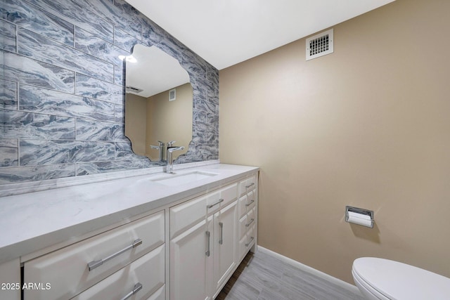 bathroom featuring vanity, toilet, baseboards, visible vents, and wood finished floors