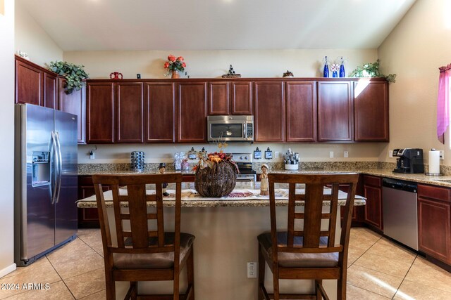 kitchen featuring a breakfast bar, appliances with stainless steel finishes, light stone counters, and light tile patterned flooring