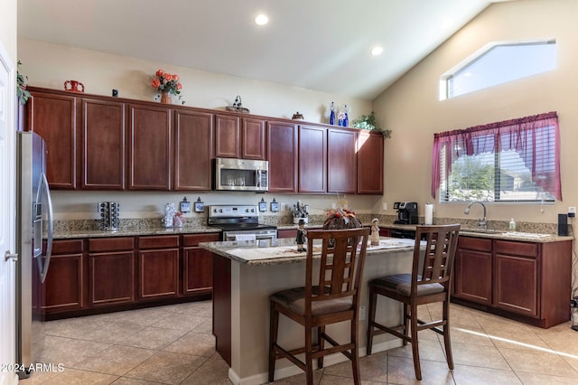 kitchen with light stone countertops, appliances with stainless steel finishes, vaulted ceiling, a kitchen island, and a breakfast bar area