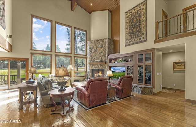 living room with wood-type flooring, a stone fireplace, high vaulted ceiling, plenty of natural light, and wooden ceiling