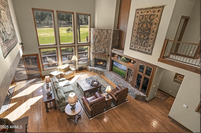 living area featuring a towering ceiling, a stone fireplace, and hardwood / wood-style floors