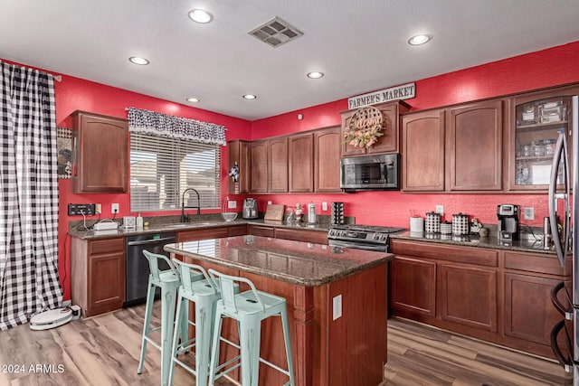 kitchen with appliances with stainless steel finishes, light wood-type flooring, a kitchen island, and sink