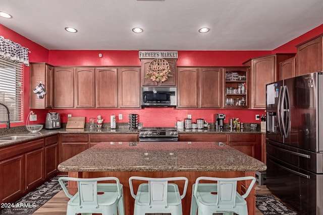 kitchen featuring dark stone counters, sink, light wood-type flooring, a kitchen bar, and stainless steel appliances