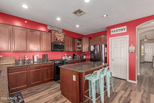 kitchen with a kitchen bar, dark stone counters, stainless steel appliances, hardwood / wood-style flooring, and a center island