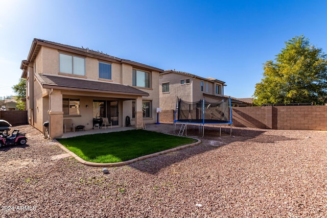 back of house featuring a lawn, a patio area, and a trampoline