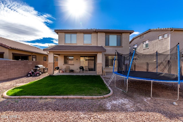 back of property with a yard, a patio, and a trampoline