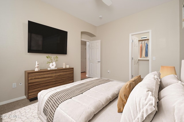 bedroom with light carpet, a spacious closet, a ceiling fan, and baseboards