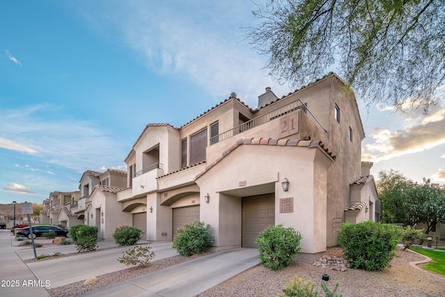 view of front facade featuring concrete driveway, a balcony, a residential view, an attached garage, and stucco siding