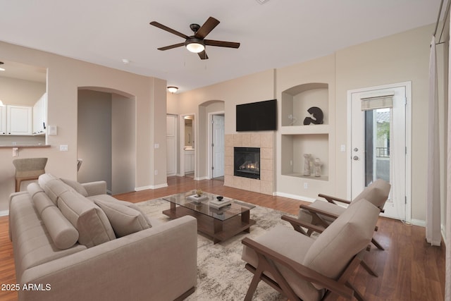 living room featuring light wood-style flooring, built in shelves, baseboards, and ceiling fan