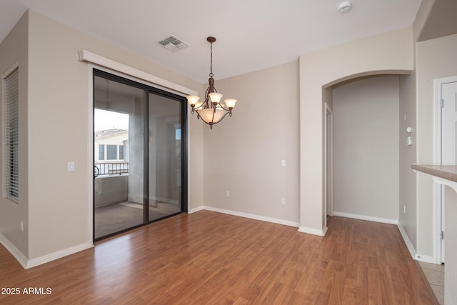 unfurnished room with baseboards, visible vents, arched walkways, wood finished floors, and a chandelier