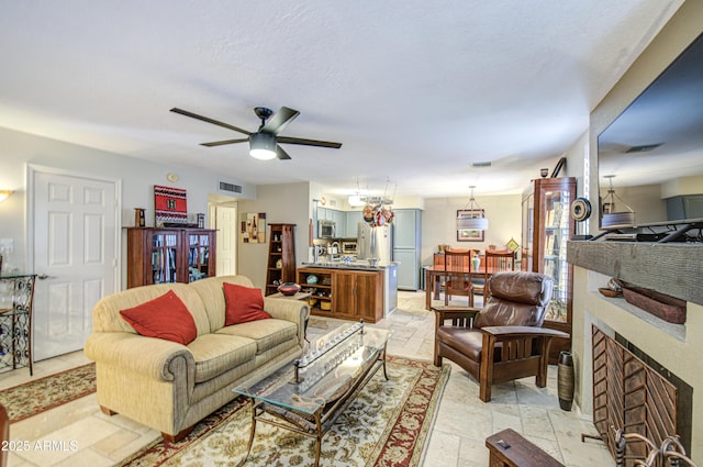 living room with stone tile floors, a ceiling fan, visible vents, and a fireplace