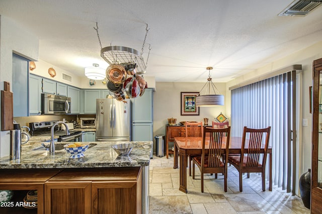 kitchen with a sink, stone countertops, stone tile floors, stainless steel appliances, and visible vents