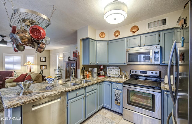 kitchen with visible vents, a peninsula, a textured ceiling, a sink, and appliances with stainless steel finishes