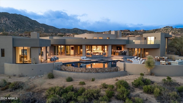 back house at dusk featuring a mountain view, a pool with hot tub, and a patio