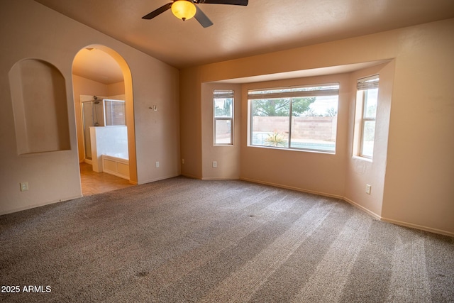 carpeted spare room with baseboards, arched walkways, and ceiling fan