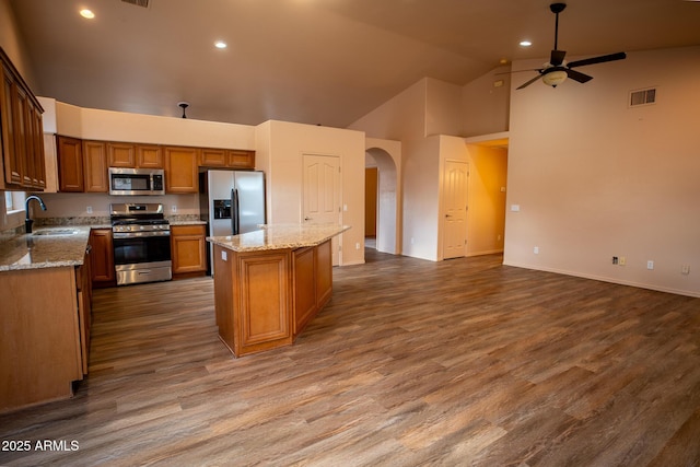 kitchen featuring arched walkways, a sink, ceiling fan, stainless steel appliances, and a center island