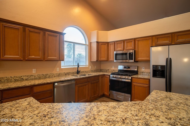 kitchen with brown cabinets, a sink, light stone counters, appliances with stainless steel finishes, and lofted ceiling