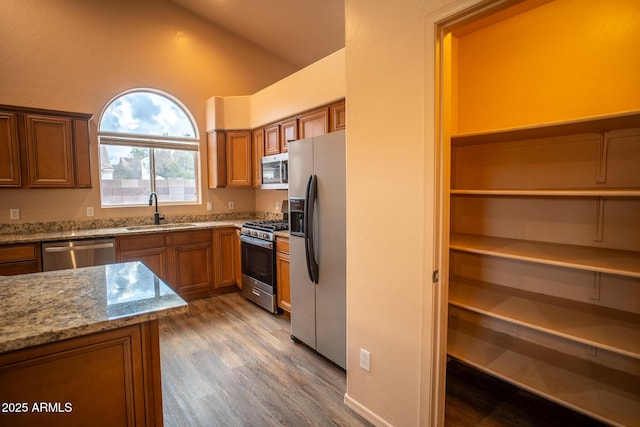 kitchen featuring brown cabinets, appliances with stainless steel finishes, lofted ceiling, and a sink